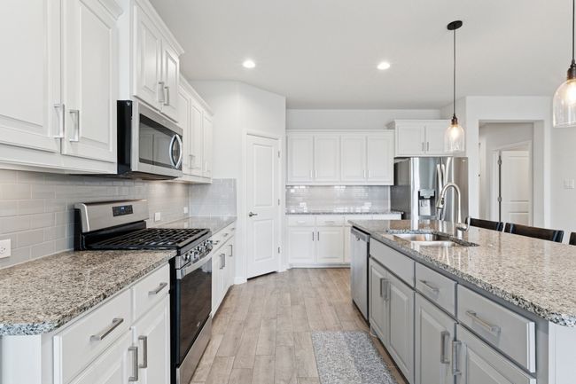 Kitchen with stainless steel appliances, white cabinetry, light wood-type flooring, a kitchen island with sink, and tasteful backsplash | Image 10