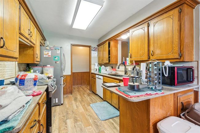 Kitchen with black microwave, electric range, dishwasher, light wood-style flooring, and brown cabinetry | Image 14