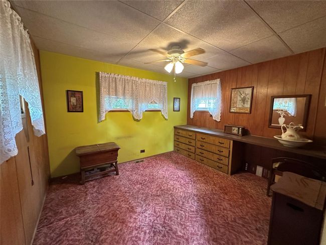 Carpeted bedroom with built in dresser with ceiling fan and wood walls | Image 12