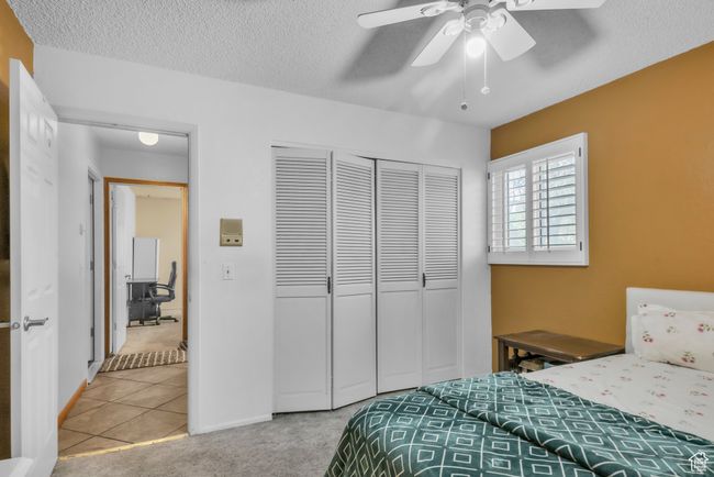 Tiled bedroom with a closet, carpet floors, a textured ceiling, a ceiling fan, and an office area | Image 18