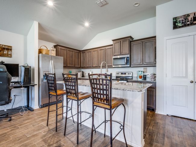 Kitchen with appliances with stainless steel finishes, dark wood finished floors, light stone counters, lofted ceiling, and a center island with sink | Image 9