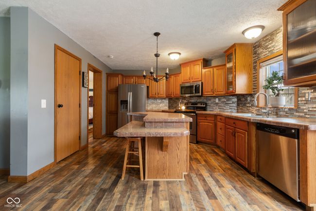 kitchen featuring tasteful backsplash, an inviting chandelier, a sink, appliances with stainless steel finishes, and brown cabinetry | Image 7