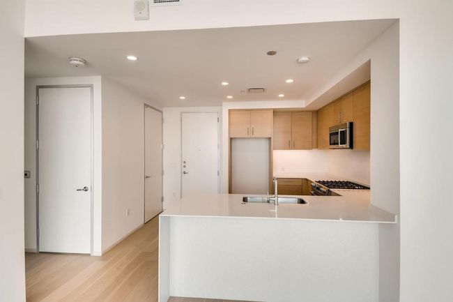 Kitchen with appliances with stainless steel finishes, a sink, a peninsula, light wood-style floors, and light countertops | Image 7