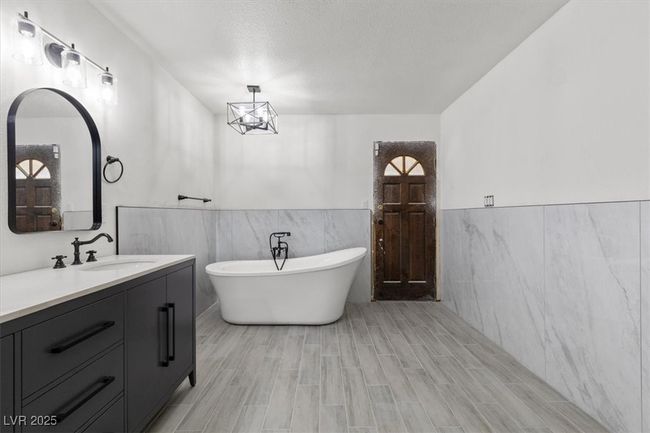 Full bathroom featuring wood finished floors, a freestanding bath, tile walls, a wainscoted wall, and vanity | Image 20