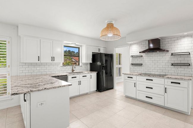 Kitchen with black appliances, wall chimney range hood, tasteful backsplash, and white cabinetry | Image 15
