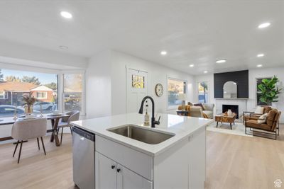 Kitchen featuring a center island with sink, stainless steel dishwasher, light hardwood / wood-style flooring, a fireplace, and sink | Image 3