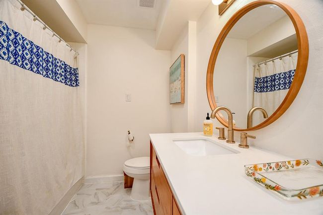 This bathroom features a modern design with a large circular mirror, elegant brass fixtures, and a stylish vanity. The shower curtain adds a pop of color with its blue pattern, complementing the neutral tones of the room. | Image 37