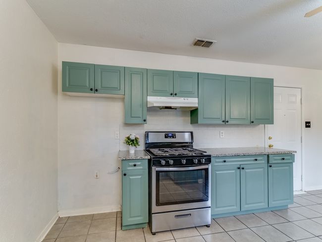 Kitchen featuring stainless steel range with gas stovetop, under cabinet range hood, light tile patterned floors, light stone counters, and decorative backsplash | Image 11