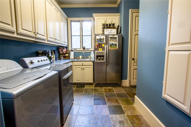 Washroom featuring washer and clothes dryer, stone tile floors, ornamental molding, a sink, and cabinet space | Image 21