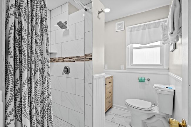 Full bathroom with toilet, wainscoting, marble look tile flooring, a stall shower, and vanity | Image 23
