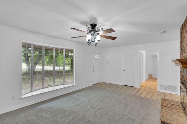 Unfurnished living room featuring light colored carpet, a brick fireplace, a ceiling fan, light tile patterned floors, and visible vents | Image 9