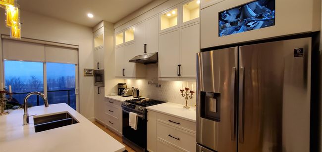 Kitchen with a sink, light countertops, white cabinets, under cabinet range hood, and stainless steel appliances | Image 11