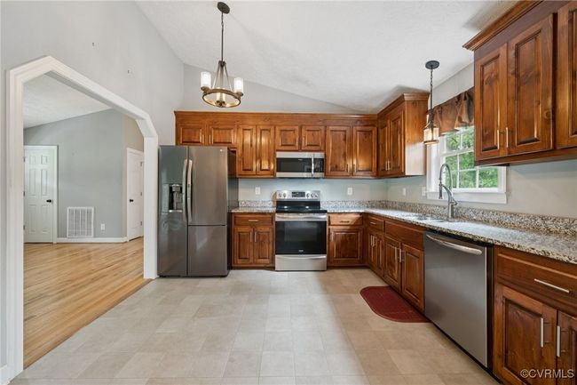 Kitchen with stainless steel appliances, a sink, lofted ceiling, a chandelier, and light stone counters | Image 16