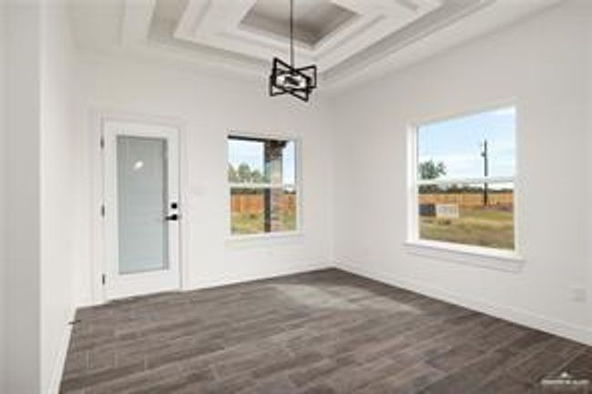 Unfurnished dining area with plenty of natural light, dark wood-style floors, a notable chandelier, and coffered ceiling | Image 8