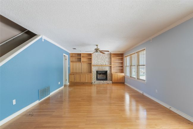 Unfurnished living room featuring a textured ceiling, ceiling fan, a fireplace, light wood-style flooring, and built in features | Image 9