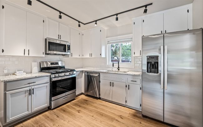 Kitchen featuring stainless steel appliances, track lighting, light stone counters, and tasteful backsplash | Image 4