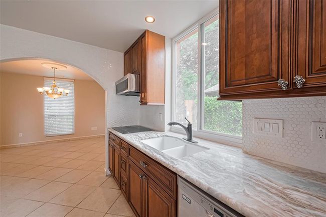 A large picture window over the sink fills the kitchen with sunlight and provides a view of the side yard. Custom cabinetry, penny tile backsplash, and updated fixtures make this a stylish and functional prep area. Wall from kitchen into dining room is all accented with tile. | Image 18
