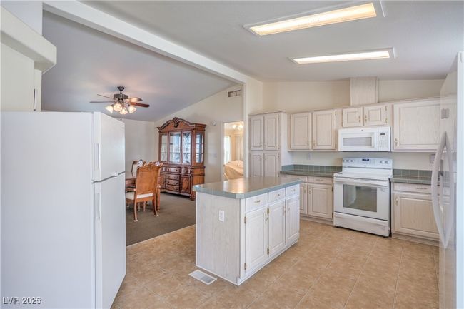 Kitchen with white appliances, light tile patterned floors, light colored carpet, ceiling fan, and a kitchen island | Image 14