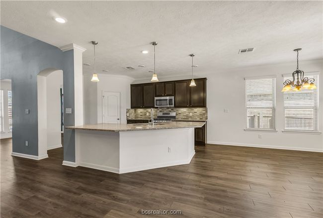 Kitchen with dark brown cabinetry, sink, a center island with sink, stainless steel appliances, and light stone countertops | Image 11