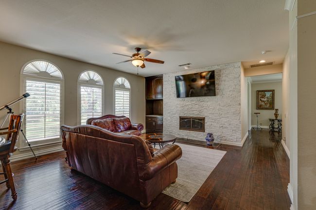 Living area featuring a fireplace surrounded by stone from floor to ceiling, ceiling fan, and dark wood-type flooring | Image 9