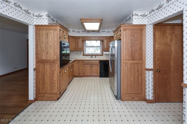 Kitchen featuring a sink, wallpapered walls, brown cabinets, light countertops, and black appliances | Image 21