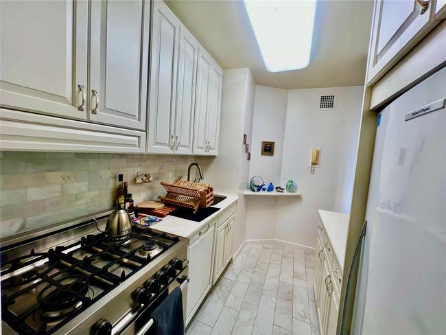Kitchen featuring gas range, light marble finish flooring, decorative backsplash, white cabinets, and ventilation hood | Image 4