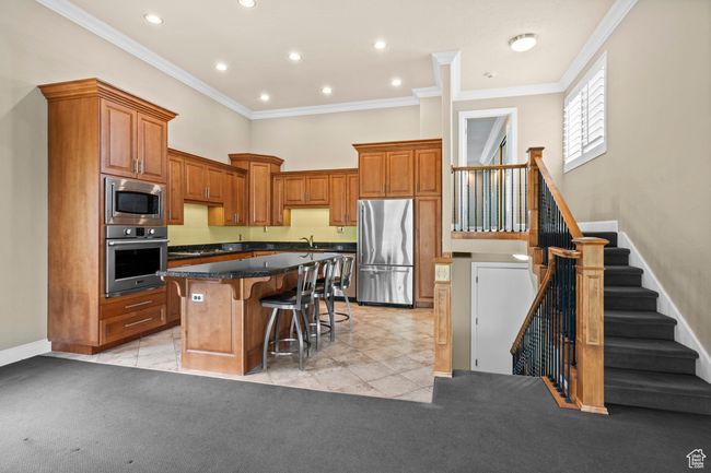 Kitchen featuring stainless steel appliances, a kitchen bar, a kitchen island, crown molding, and a towering ceiling | Image 16
