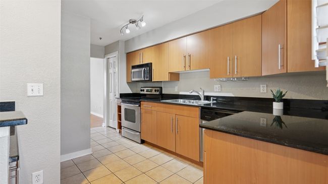 Kitchen with appliances with stainless steel finishes, a sink, light tile patterned floors, baseboards, and dark stone countertops | Image 13