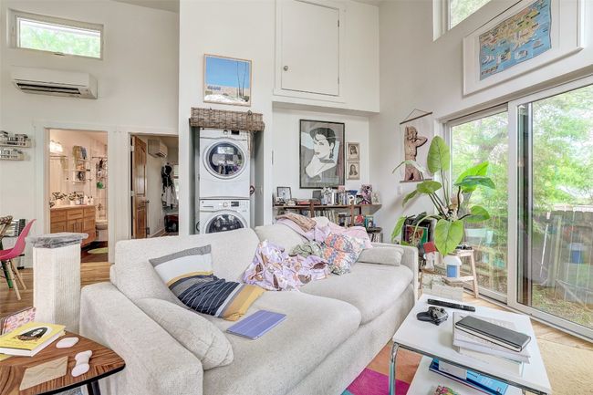 Living area featuring a wall mounted AC, wood finished floors, stacked washer and dryer, and a high ceiling | Image 40