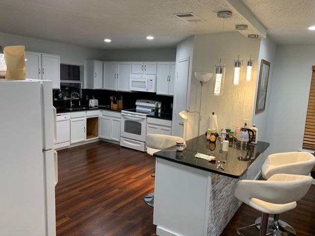 Kitchen featuring white appliances, dark countertops, white cabinets, a sink, and dark wood-style flooring | Image 23