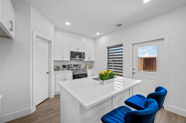 Kitchen featuring stainless steel appliances, light wood-type flooring, white cabinets, light stone countertops, and an island with sink | Image 9