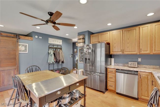 Kitchen featuring stainless steel appliances, stainless steel counters, a ceiling fan, light brown cabinets, and a barn door | Image 12