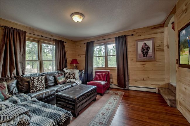 Living room featuring baseboard heating, wooden walls, wood finished floors, and a textured ceiling | Image 18