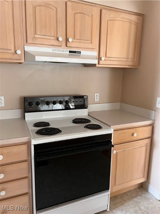 Kitchen featuring range, wall chimney exhaust hood, light brown cabinetry, and light countertops | Image 4