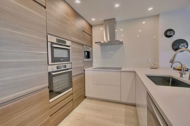 Kitchen with modern cabinets, wall chimney exhaust hood, appliances with stainless steel finishes, light countertops, and light wood-type flooring | Image 4
