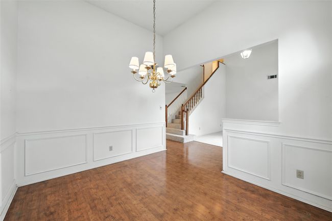 Unfurnished dining area with a decorative wall, a chandelier, vaulted ceiling, wood finished floors, and stairs | Image 6