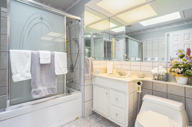 Bathroom featuring marble finish floors, shower / bath combination with glass door, vanity, toilet, and tile walls | Image 20