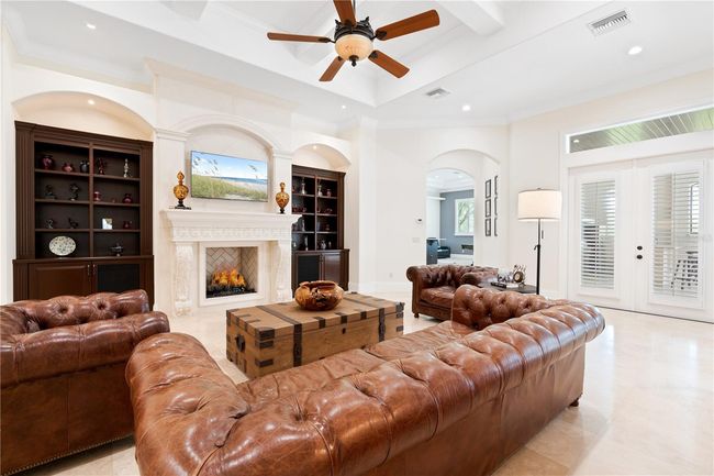 The elegant family room features soaring ceilings, a grand fireplace with custom stonework, and built-in cabinetry, creating a warm and sophisticated space for gathering and entertaining. | Image 5