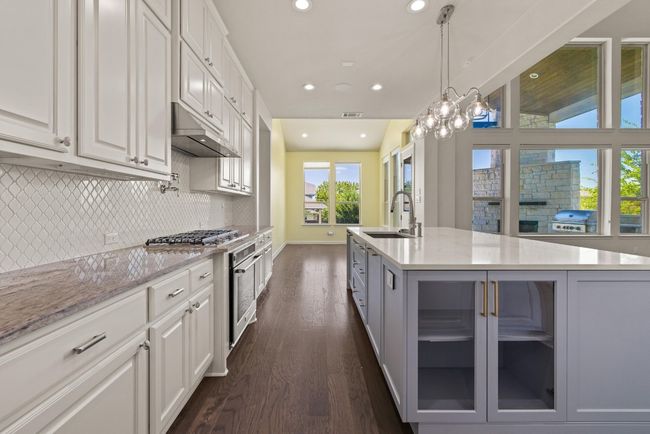 Kitchen with under cabinet range hood, dark wood-type flooring, recessed lighting, decorative backsplash, and white cabinetry | Image 6