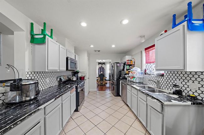This kitchen offers a functional layout with generous cabinet storage, updated countertops, and sleek finishes throughout. Freshly installed in 2024, the Whirlpool stainless steel gas range and oven provide high-performance cooking, complemented by a matching built-in microwave and dishwasher. A striking black-and-white tile backsplash adds visual contrast and character, tying the space together with a clean, modern feel. | Image 9