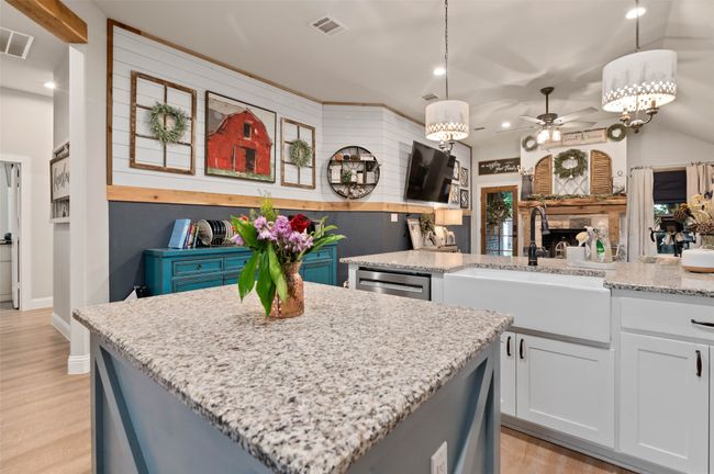 Kitchen with a kitchen island, ceiling fan, light stone counters, light wood-style flooring, and decorative light fixtures | Image 9