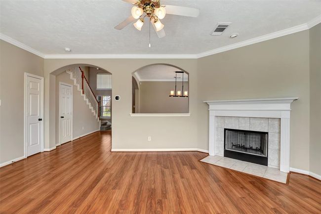 This inviting living room features hardwood floors, a cozy fireplace, and a ceiling fan. Arched doorways lead to other areas, adding elegance, and there's a view of the staircase, enhancing the open layout. | Image 14