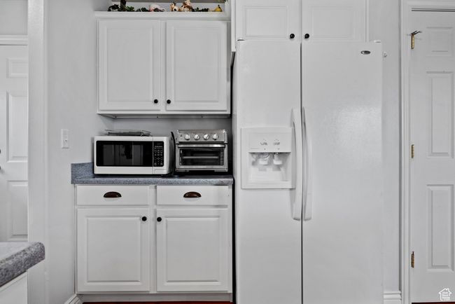 Kitchen with white cabinetry, dark countertops, a toaster, and white appliances | Image 10