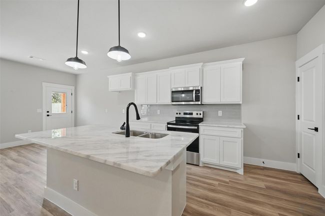 Kitchen featuring tasteful backsplash, appliances with stainless steel finishes, white cabinetry, a sink, and light wood-style floors | Image 6