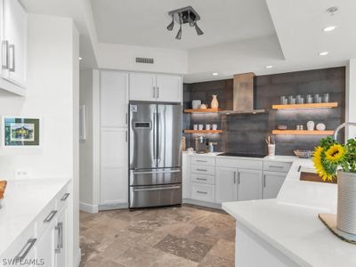 Kitchen with wall chimney exhaust hood, stainless steel fridge, white cabinetry, and light tile floors | Image 1