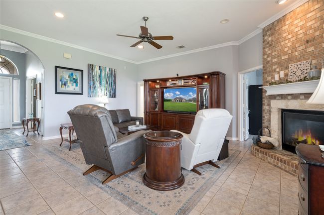 Living area featuring ceiling fan, arched walkways, light tile patterned floors, ornamental molding, and a brick fireplace | Image 15