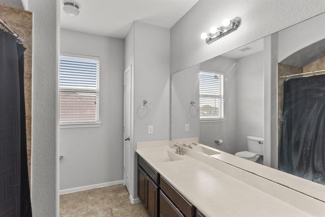 Lovely secondary bathroom complete with a large mirror, granite countertops and wooden cabinets, and a shower/tub combo with a gorgeous tile shower wall. | Image 17
