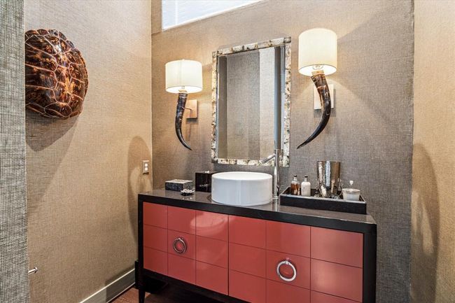 The handsomely appointed formal POWDER ROOM includes wide plank hardwood flooring, furniture style cabinet with vessel sink, decorative mirror, textured wallpaper, wall mounted light sconces (cattle horn theme), raised horizontal privacy window with shade, recessed lighting, base molding. | Image 19