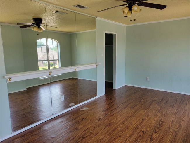Empty room with a ceiling fan, a textured ceiling, wood finished floors, and crown molding | Image 15