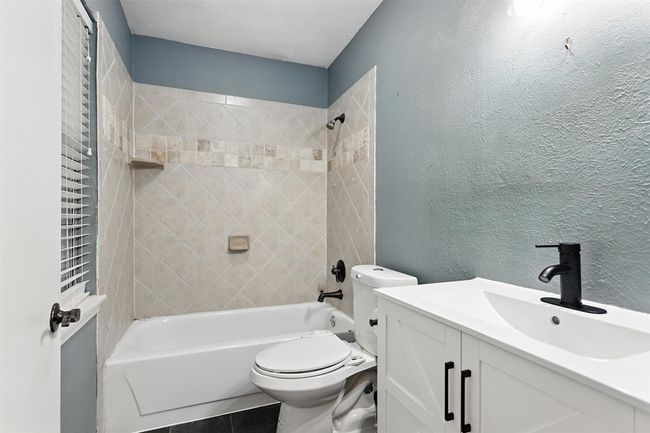 Bathroom with vanity, tub / shower combination, a textured wall, and tile patterned floors | Image 16